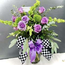 Purple roses in a glass vase with black-and-white checkered ribbon and a purple bow