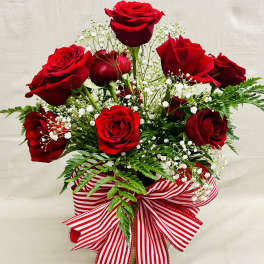 Red roses arranged in a vase with baby's breath and a striped ribbon