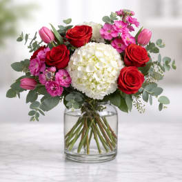 Bouquet of red roses, pink tulips, and white hydrangea in a glass vase