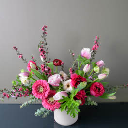 Low floral arrangement with pink roses and red blooms in a dark container