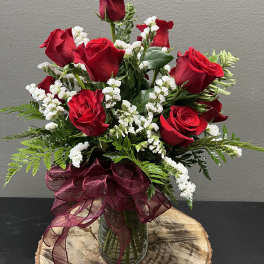 Red roses arranged in a glass vase with white filler flowers and a burgundy ribbon