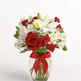 Red roses and white lilies arranged in a glass vase with a red ribbon