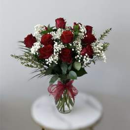 Clear glass vase of red roses with white filler flowers and a red bow.