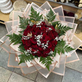 Bouquet of red roses with baby's breath and fern foliage in layered pink wrap