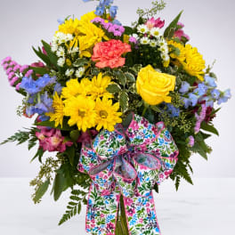 Bright mixed bouquet in a glass vase with a floral ribbon.