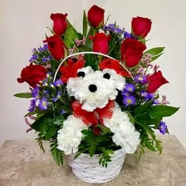 Basket arrangement of red roses, white daisies, and purple flowers