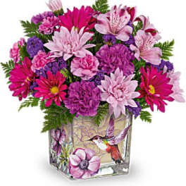 Bright pink and purple mixed flower arrangement in a square glass vase with a hummingbird illustration
