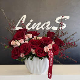 Red and blush roses arranged in a white vase with a red ribbon