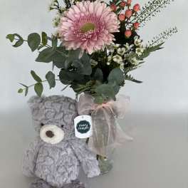 Pink gerbera bouquet in a glass vase with a gray teddy bear