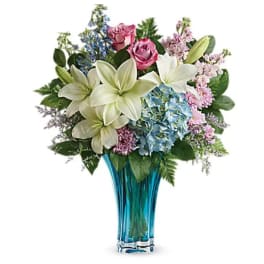 Bouquet of lilies, roses, and hydrangeas in a blue glass vase