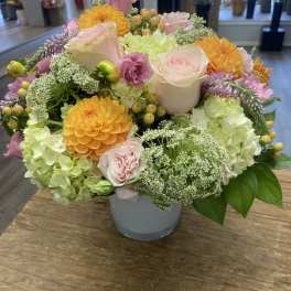 Mixed pastel bouquet in a gray vase with roses, hydrangeas, and orange blooms