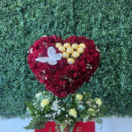 Heart-shaped red carnation arrangement with chocolates and a butterfly topper