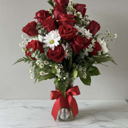 Red roses and white daisies arranged in a glass vase with a red ribbon.