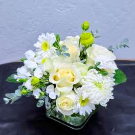 White and pale yellow floral arrangement in a square glass vase