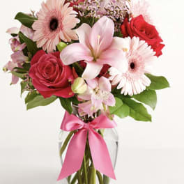 Pink and red mixed bouquet in a glass vase with a pink ribbon