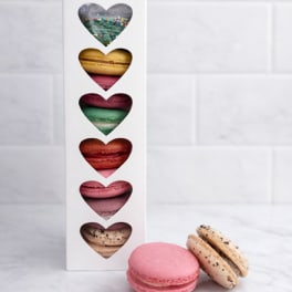 Box of assorted heart-shaped macarons with two macarons in front