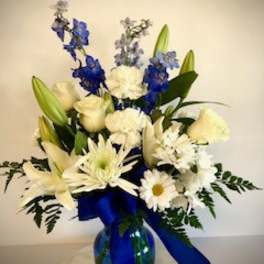 White and blue floral arrangement in a glass vase with a blue ribbon