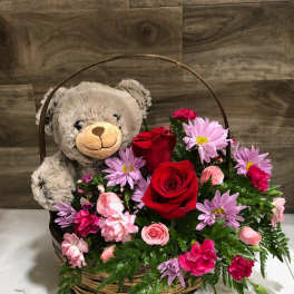 Teddy bear in a basket with red roses and pink flowers