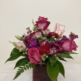Pink and purple rose bouquet in a square vase with a small love card