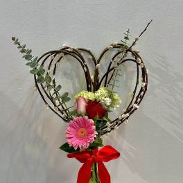 Heart-shaped floral arrangement with roses, gerbera daisy, and a red ribbon