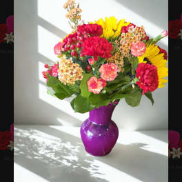 Mixed bouquet of red, pink, and yellow flowers in a purple vase