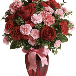 Red roses and pink carnations in a red vase with a pink ribbon