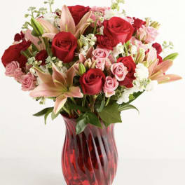 Red and pink roses with lilies in a red glass vase