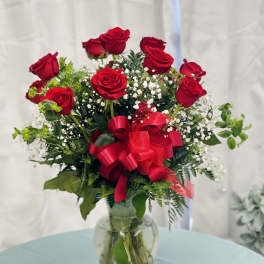 Red roses arranged in a glass vase with a red ribbon