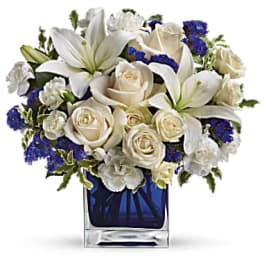 White lilies and roses in a blue glass vase with purple accents