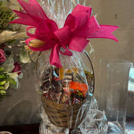 Basket of assorted chocolates wrapped in clear cellophane with a bright pink bow