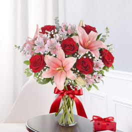 Bouquet of red roses and pink lilies in a glass vase with a red ribbon