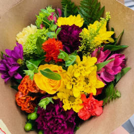 Colorful mixed bouquet with yellow, purple, pink, and orange flowers wrapped in brown paper