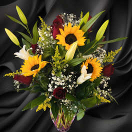 Bouquet of sunflowers, red roses, and white lilies in a glass vase