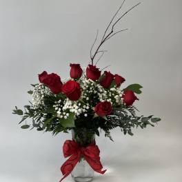 Red roses arranged in a glass vase with baby's breath and a red bow
