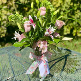 Pink roses and lilies arranged in a glass vase with a floral ribbon