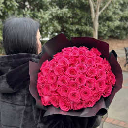 Person holding a large bouquet of bright pink roses wrapped in black paper