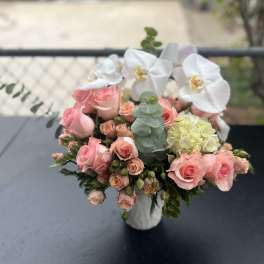 Pink roses and white orchids arranged in a white vase