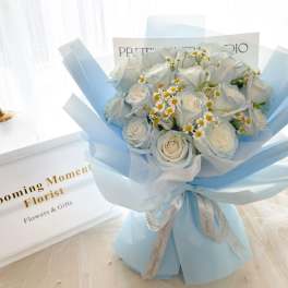 Bouquet of white roses and small daisies wrapped in pale blue paper