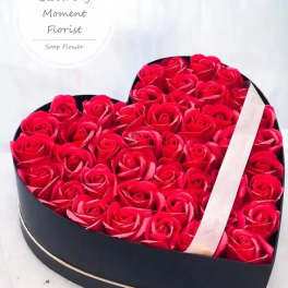 Heart-shaped box filled with red roses and a ribbon