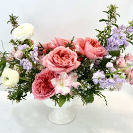 Pink and lavender roses arranged in a white pedestal vase