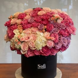 Large round arrangement of pink and lavender roses in a black hat box