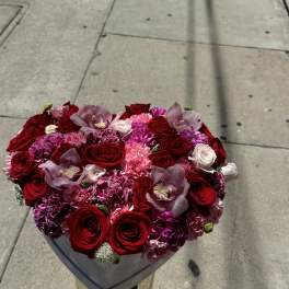 Heart-shaped bouquet of red roses, pink carnations, and orchids