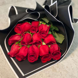 Dozen red roses wrapped in black paper with white trim on a stone surface