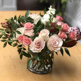 Pink and white roses arranged in a glass vase with greenery