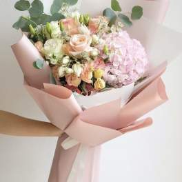 Hand-tied bouquet of pink and cream flowers wrapped in blush paper
