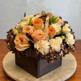 Peach and cream roses arranged in a square box with a ribbon