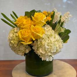 Yellow roses and white hydrangeas in a green glass vase