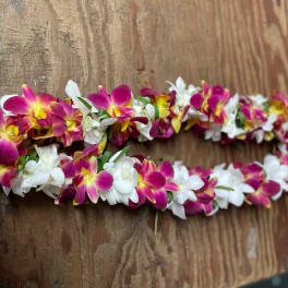 Two floral leis made of pink, yellow, and white orchids on a wooden surface