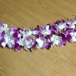 Purple and white orchid lei laid on a wooden surface