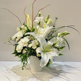 White lilies and small white flowers arranged in a white vase